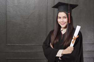 Portrait of young woman in graduation gown smiling and cheering on black background photo