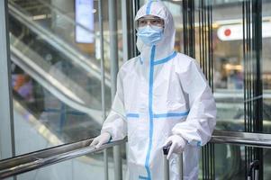 un hombre asiático lleva traje de ppe en el ascensor del aeropuerto, viajes de seguridad, protección covid-19, concepto de distanciamiento social foto