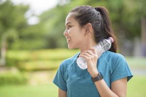 Fitness woman is drinking water after workout in park photo