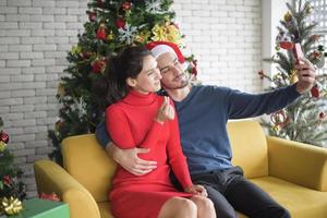 Attractive Caucasian couple of love are  celebrating Christmas in home, making video call to family via smart phone photo