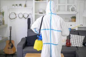 A medical staff in PPE suit is using disinfectant spray in living room, Covid-19 protection , disinfection concept . photo