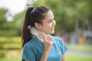 Fitness woman is drinking water after workout in park photo