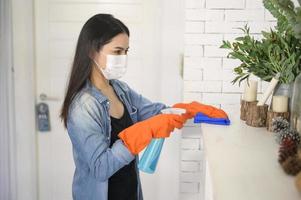 una mujer con guantes de limpieza que usa desinfectante en aerosol de alcohol para limpiar la casa, saludable y médica, concepto de protección covid-19 en el hogar foto