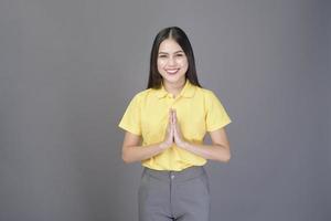 beautiful confident woman is greeting Thai wai to show respect over grey background studio photo