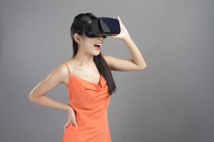 Fashion portrait of beautiful woman in orange dress is wearing a virtual reality box isolated over gray background studio. photo