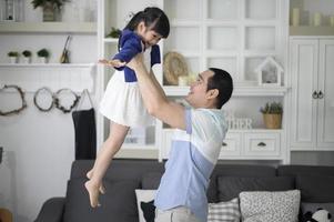 un padre sano sostiene a una linda hija feliz volando y jugando al avión juntos en casa los fines de semana, concepto familiar. foto