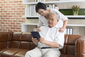 A happy senior Asian couple is using tablet and talking with family on webcam at home, retirement concept. photo