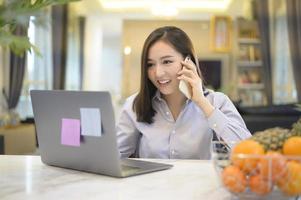 una hermosa mujer de negocios asiática está trabajando con su computadora en casa, telecomunicaciones, distanciamiento social, concepto de trabajo desde casa
