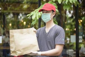 un repartidor asiático lleva mascarilla, sostiene una bolsa de comestibles, concepto de entrega a domicilio de seguridad