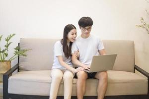 a young happy couple is relaxing and using a laptop on a sofa at home photo