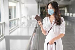 A traveller woman is wearing protective mask in International airport, travel under Covid-19 pandemic, safety travels, social distancing protocol, New normal travel concept photo