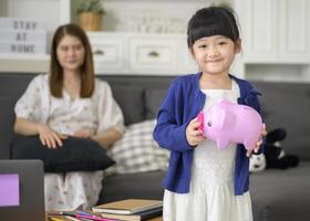 una familia asiática le está enseñando a su hija a ahorrar dinero con una alcancía, concepto de planificación financiera foto