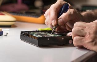 electronic engineer repairs computer hard drive. technologist with a screwdriver disassembles hdd photo