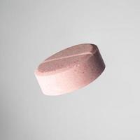 one pink medical ascorbic pill on light grey background. Isolated photo