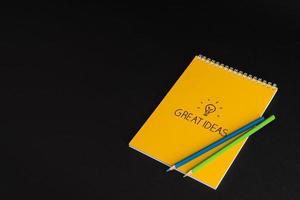 yellow notepad with colored pencils on black background, isolated. back to school. great ideas photo