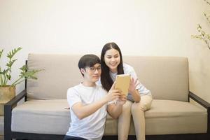 a happy couple wearing blue shirt is relaxing and holding a tablet on a sofa at home photo