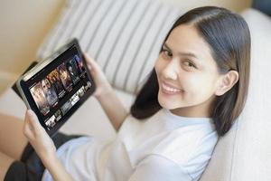 una mujer joven está usando la aplicación netflix en una tableta en su casa, netflix es una aplicación de entretenimiento popular en tailandia foto