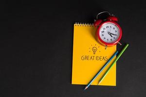 alarm clock with notepad and colored pencils on black background, isolated. back to school. great ideas photo