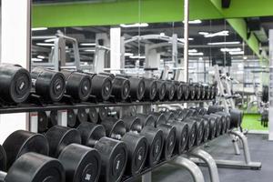 close up black sport dumbbells lie in a row on a stand photo