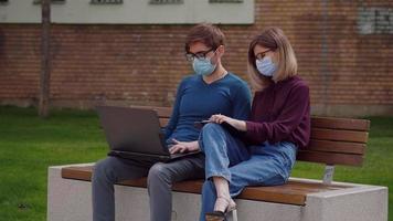 Two coworkers in protective mask discuss concentrating typing on laptop. video