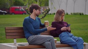 la femme et l'homme s'assoient sur le banc tout en sirotant une pause-café à emporter video