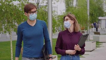 Two work colleagues in protective mask walk outside office building.