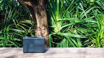 Black business leather briefcase, handbag with key lock at office, on wooden surface with green nature background photo