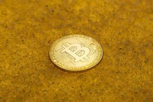 one bitcoin crypto coin on a shiny golden sand background with backlight photo