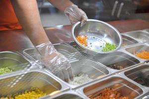 cook puts pieces of vegetables for salad in a bowl. tray with assorted for salad in the window of a fast food restaurant photo