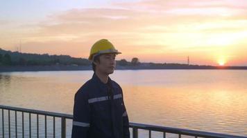 een mannelijke ingenieur die een beschermende helm draagt bij zonsondergang. video