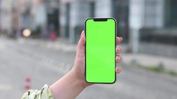 mujer sosteniendo el teléfono en la mano con pantalla verde en la calle