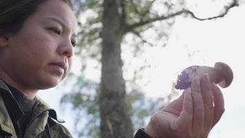 Close up Asian woman holding a mushroom in her hand in forest, standing and looking at mushroom on her hand, going out in a forest on the weekend. Being in the beautiful nature video