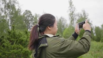 mujer asiática tomando una foto en una hermosa granja, saliendo en una granja, usando un teléfono inteligente para tomar una foto y tomando aire fresco el fin de semana, relajando el estado de ánimo en un concepto de granja