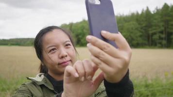 mujer asiática tomando selfies, saliendo a una granja, usando un smartphone para tomarse una foto con una hermosa vista y tomando aire fresco el fin de semana, relajando el estado de ánimo en un concepto de granja video