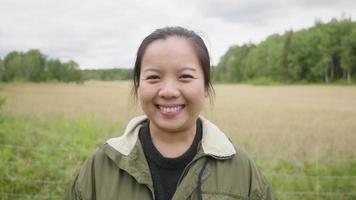 Vorderansicht der asiatischen Bäuerin, die auf der grünen Wiese steht, Porträt einer Landarbeiterin in der Landwirtschaft, lächelnd und mit Blick auf die Kamera. fröhliche stimmung in einem farmkonzept video