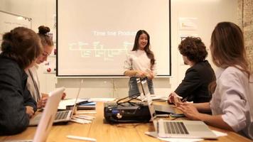 A cute Asian female staff standing and presenting business marketing strategy to her boss and multiracial colleagues, confident speaking in brainstorming meeting conference room at corporate office. video