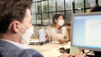 Multiracial coworkers team with face mask working in new normal office. COVID-19 protection by cleared partition, business workplace office, social distancing for pandemic health, disease prevention.