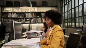 Busy female worker, young African American staff is hard working with a lot of stack of documents and paperwork on desk, overload worked tirelessly for the job deadline in business office workspace.