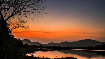 Landscape with orange and purple at sunset  silhouettes of mountains, hills and forest lake photo