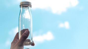Male Hand hold transparent glass bottle. Empty bottle fill with blue sky. Against blue sky. Empty copy space. Clean air environment nature for life concept idea background photo