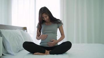 schwangere frau, die morgens auf dem bett sitzt und den bauch berührt video