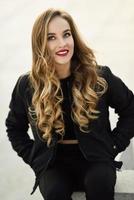 Beautiful young girl wearing black jacket sitting in the street. photo