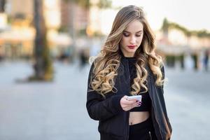 mujer rubia enviando mensajes de texto con su teléfono inteligente en un entorno urbano foto