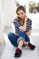 Blonde woman, model of fashion, sitting in urban background.
