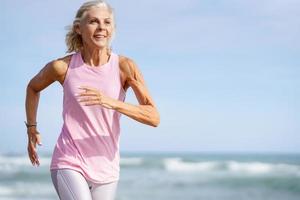 mujer mayor haciendo deporte para mantenerse en forma. mujer madura corriendo por la orilla de la playa. foto