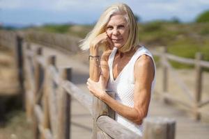 Happy female in her 60s leaning on wooden fences on the sand of a tropical beach. photo