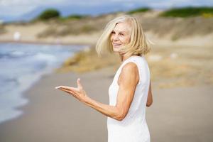 Smiling mature woman walking on the beach, spending her leisure time, enjoying her free time photo
