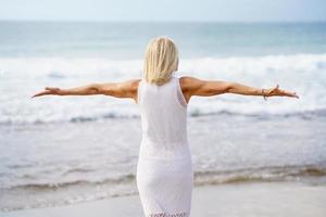 Mature woman opening her arms on the beach, spending her leisure time, enjoying her free time