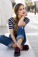 Blonde woman, model of fashion, sitting in urban background.