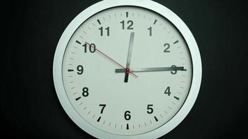 White wall clock tells the time of noon and 15 minutes.   Time walks slowly in a day on black background. video